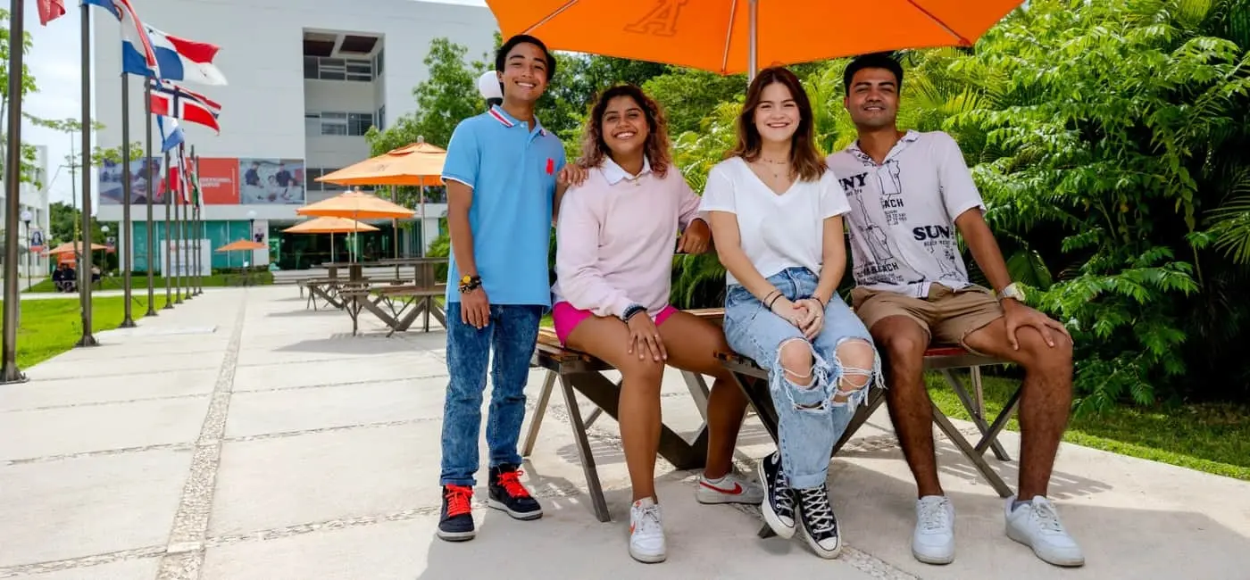Grupo de estudiantes universitarios internacionales conviviendo al aire libre en campus sustentable con banderas y áreas verdes.