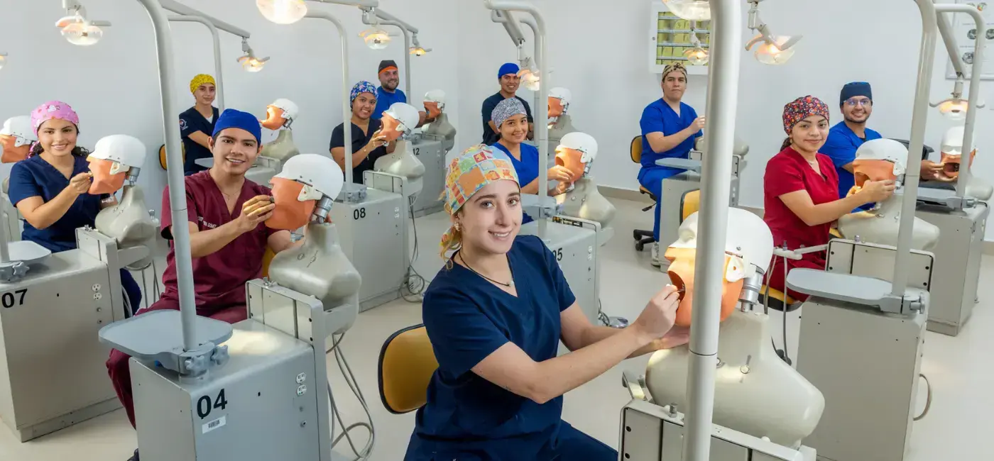 Grupo de estudiantes de odontología practicando procedimientos en maniquíes de entrenamiento dental dentro de un laboratorio de simulación moderno de la universidad.